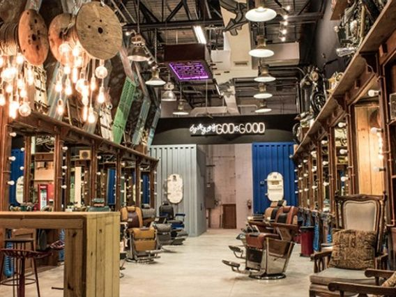 Interior of a vintage-themed barbershop with multiple barber chairs, wooden floors, and eclectic lighting fixtures.